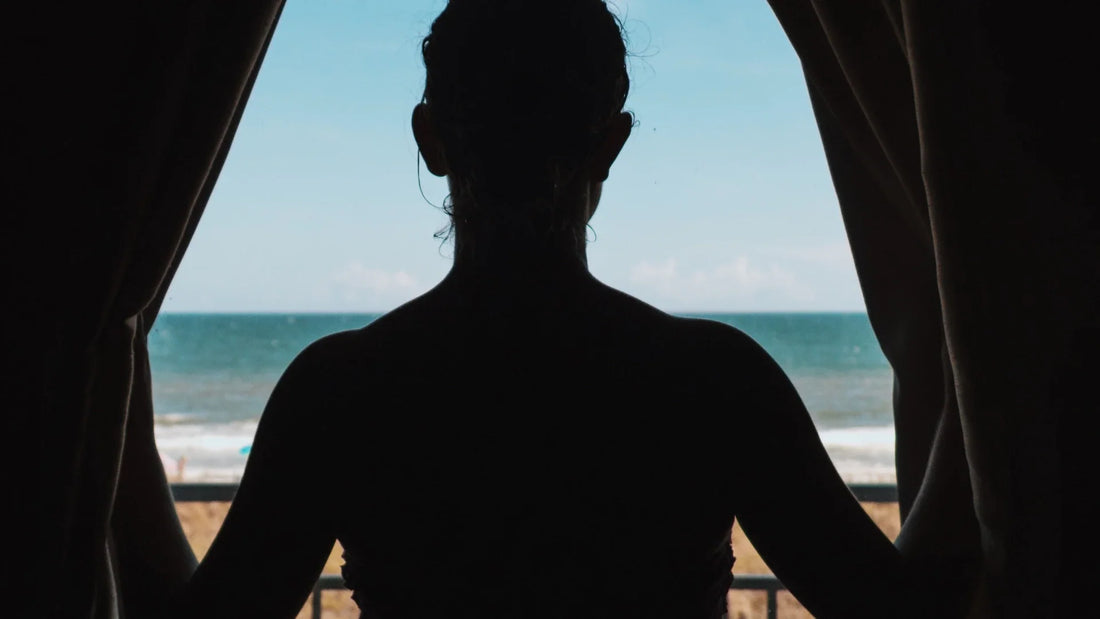 An adult woman seen from behind as a dark silhouette between curtains.