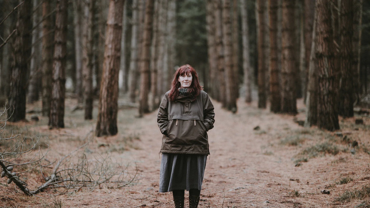 A woman in a green jacket stands on a woodland path.