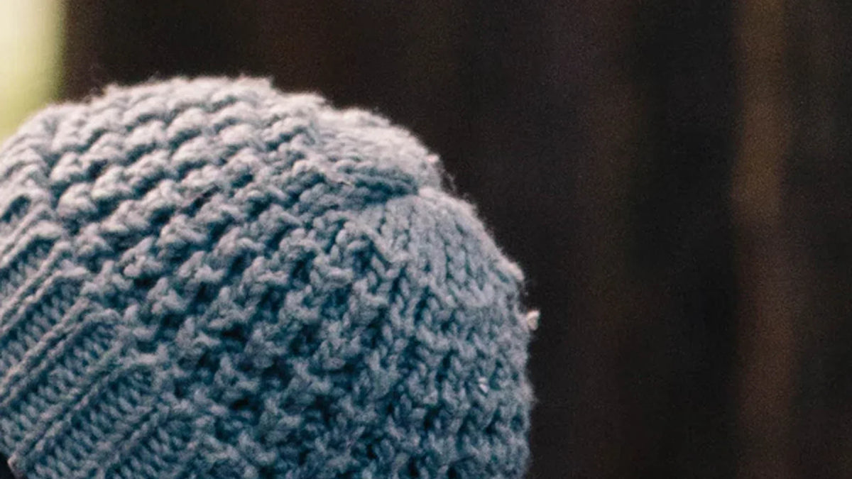 The back of a knitted hat and scarf against a softly focused forest.