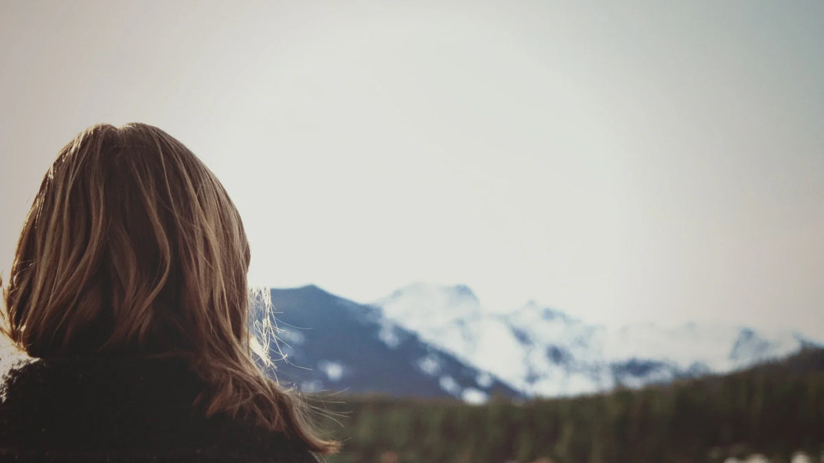 An adult woman viewed from behind in a mountain landscape.