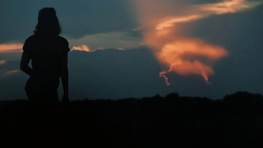 A woman is silhouetted against the sky at sunset.