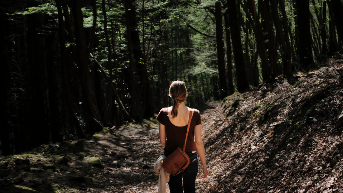 An adult woman walking along a forest path, viewed from behind.