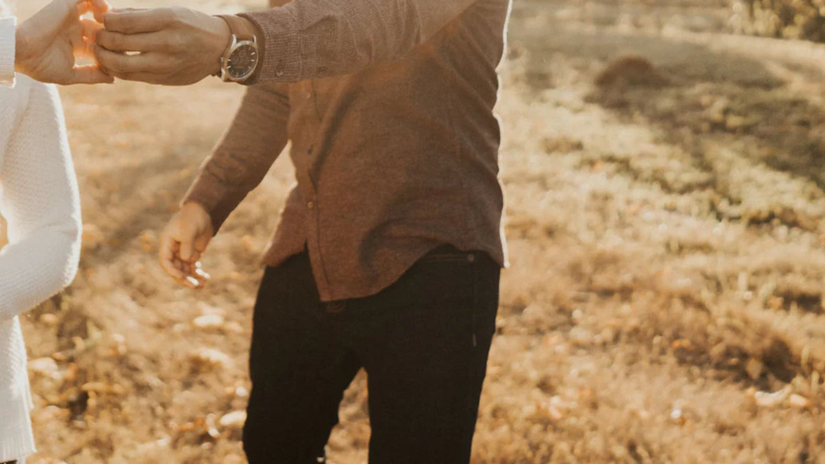 A couple holding hands outdoors, cropped below their faces.