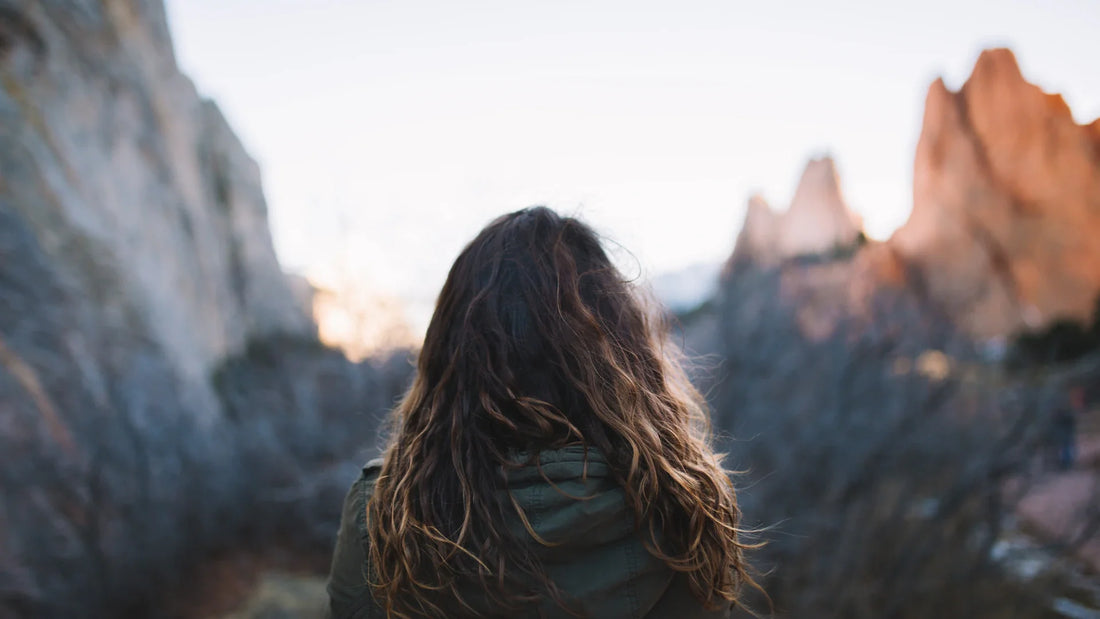 An adult woman viewed from behind in a mountain landscape.