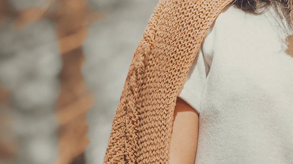 A close view of an adult woman’s knitted cardigan and white blouse against a softly focused forest.