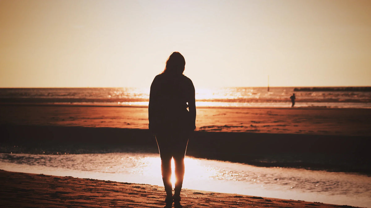 An adult woman silhouetted beside the sea.