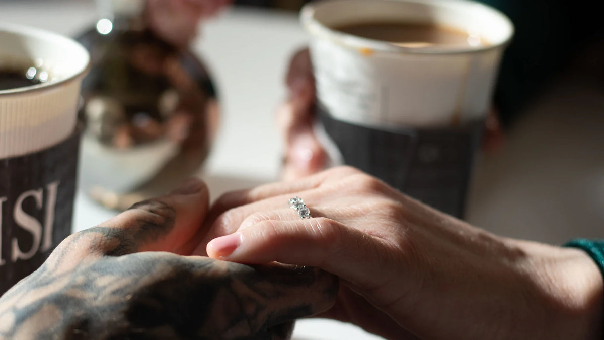 Two hands meet beside a cup of coffee.