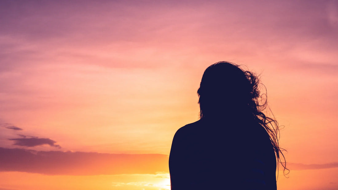 An adult woman in silhouette, viewed from behind outdoors.