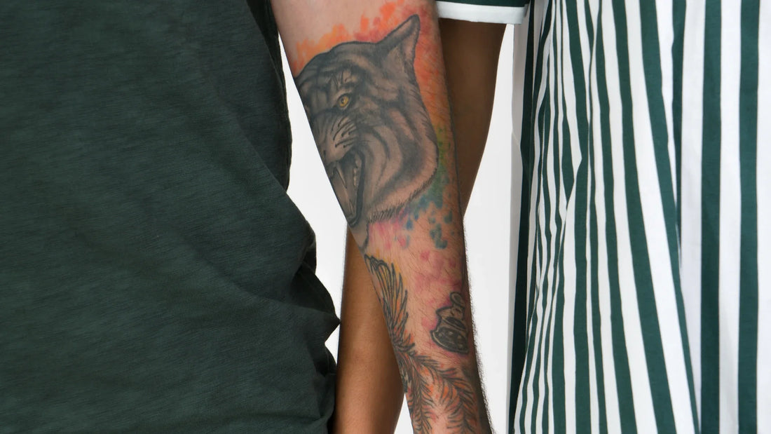 A close view of two adult arms, one tattooed, beside striped clothing.