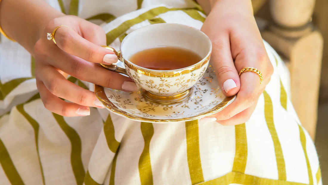 An adult woman holding a patterned teacup and saucer, with her face outside the frame.