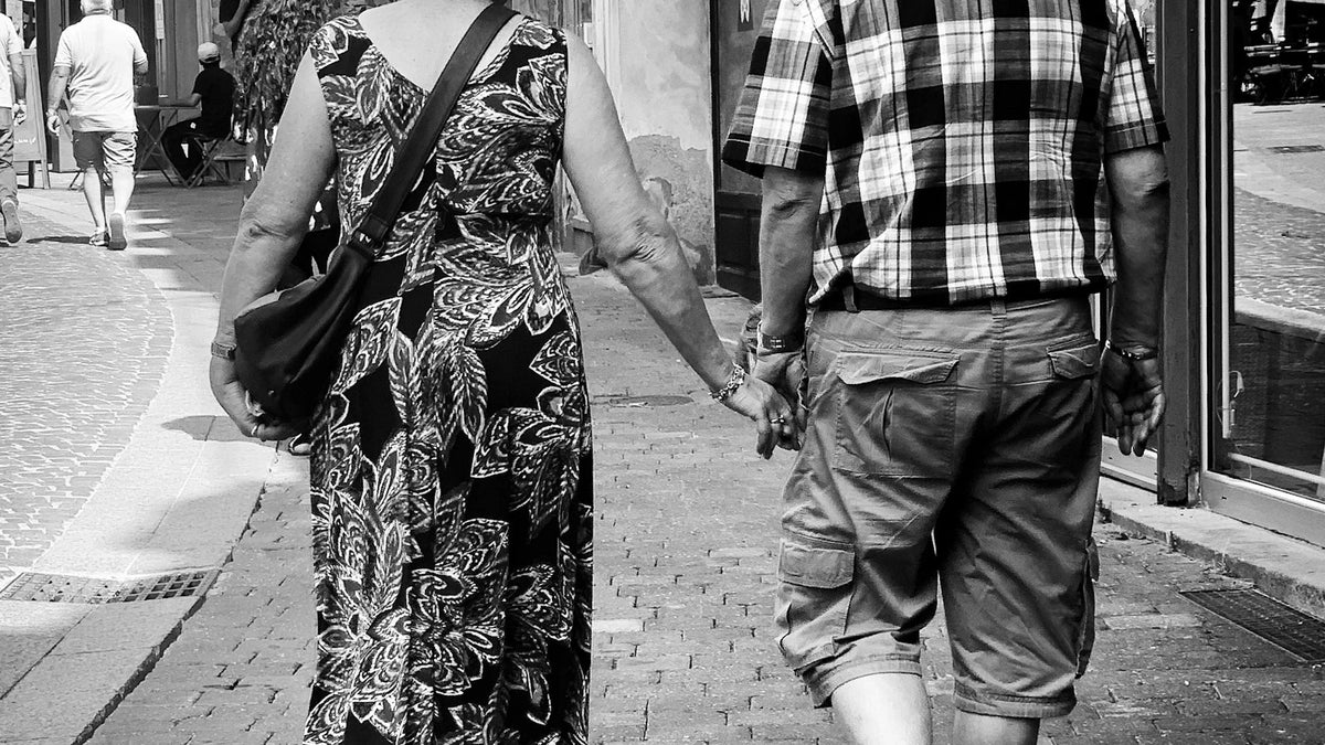 Adult companions viewed from behind while walking outdoors.