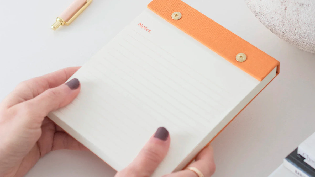 Hands hold a notebook at a desk.