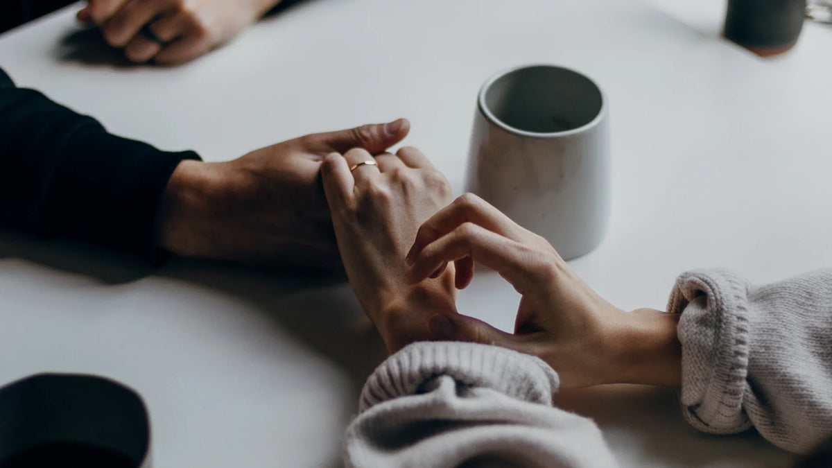 Two people holding hands across a table during a conversation.
