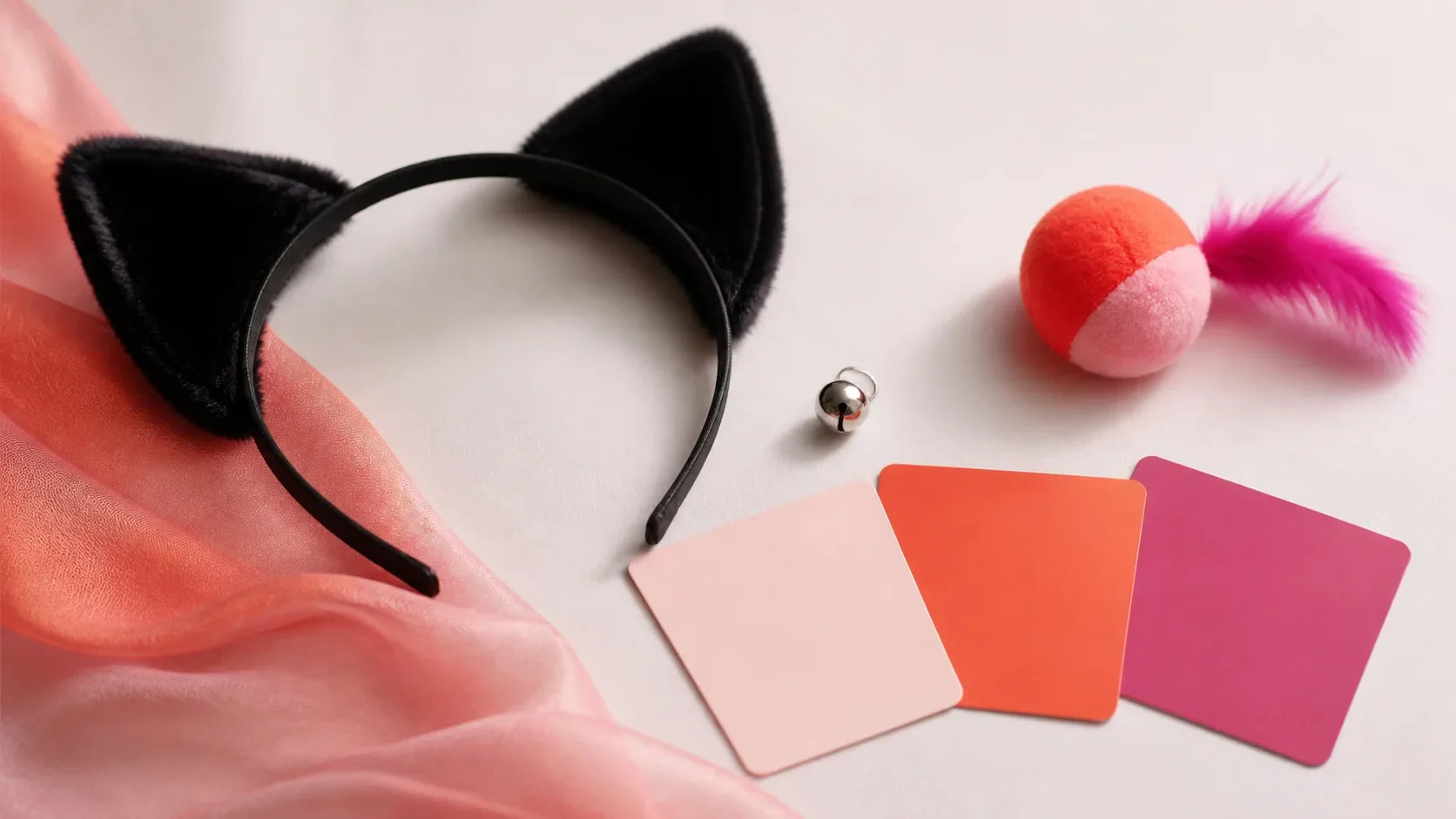 Black cat-ear headband, silver bell, soft toy and blank boundary cards on a coral and magenta studio background