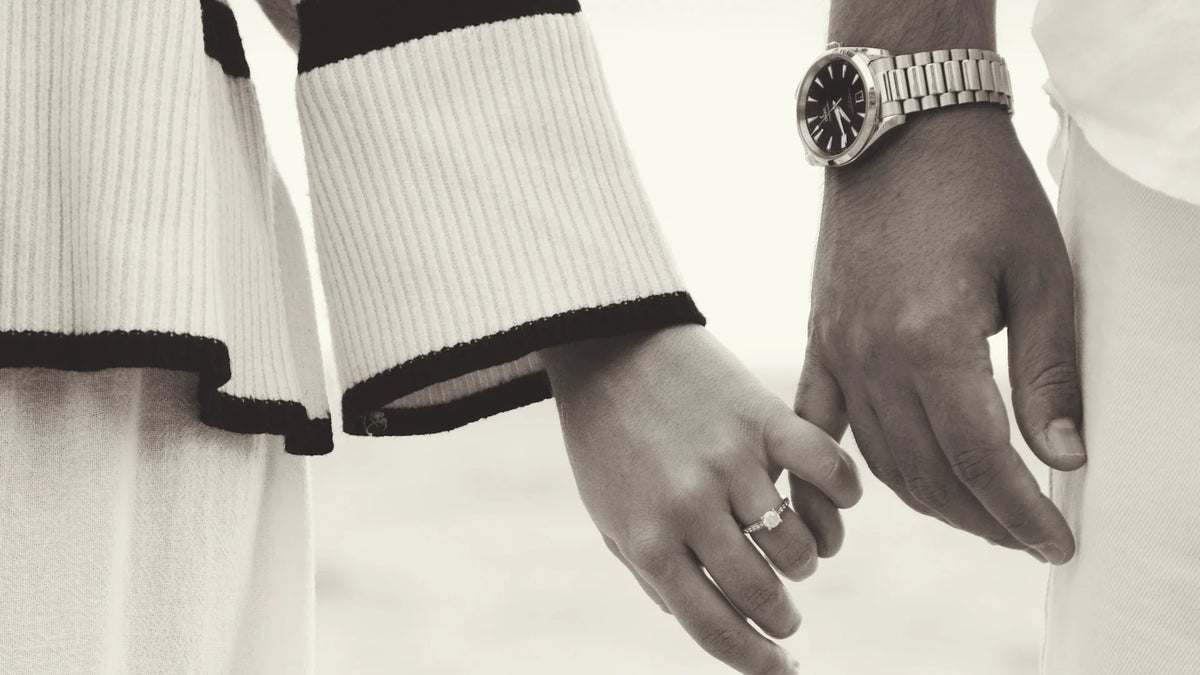 A black-and-white close-up of a couple gently linking hands.