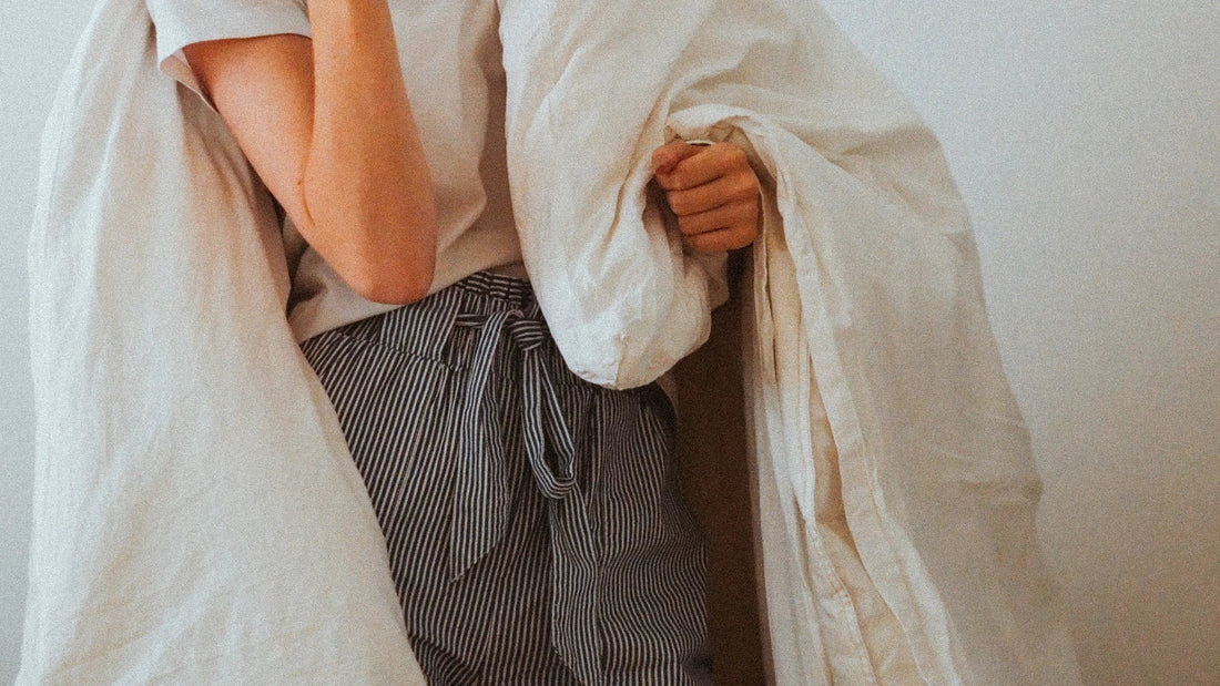 A woman wrapped in white bedding during a quiet moment at home.