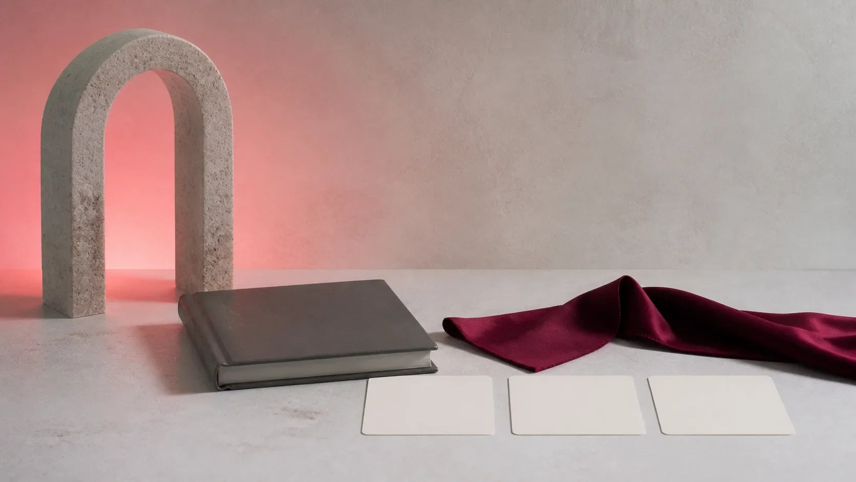Stone arch, unmarked closed book, burgundy ribbon and blank boundary cards in a coral-lit studio