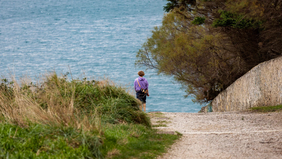 A woman viewed from behind walking beside the sea.