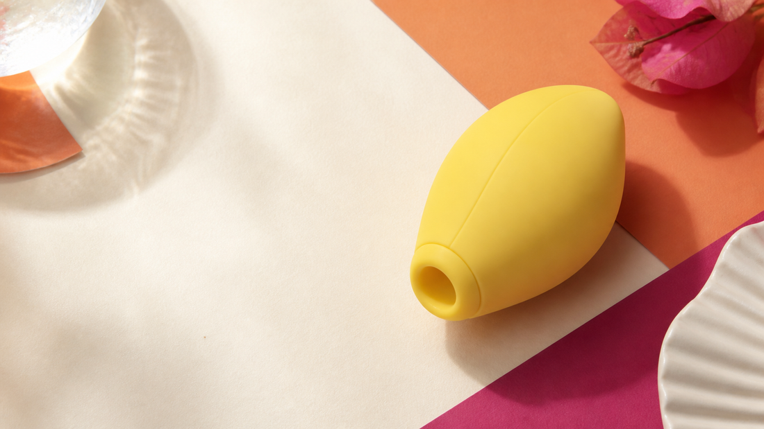 Unbranded yellow lemon-shaped external wellness device on an ivory and coral studio surface.