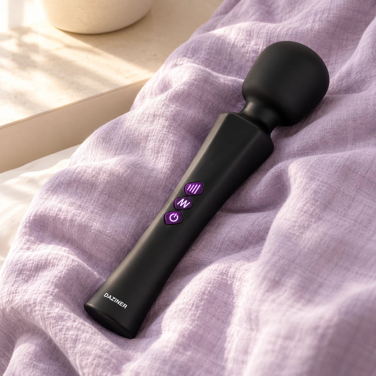 Black Aura wand resting on lilac linen in warm natural window light